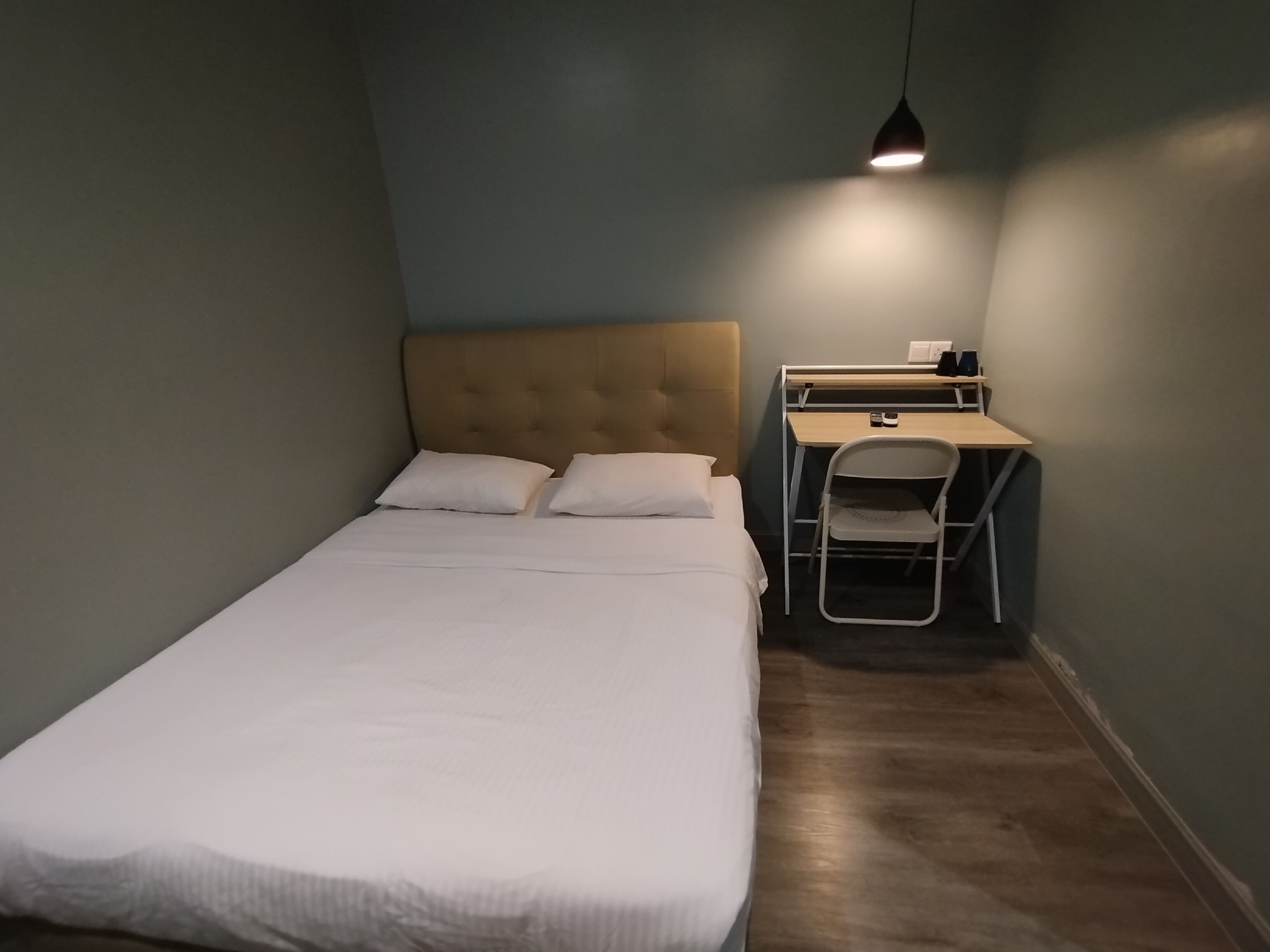 A small, neatly arranged room with a single bed, a desk, and a chair.