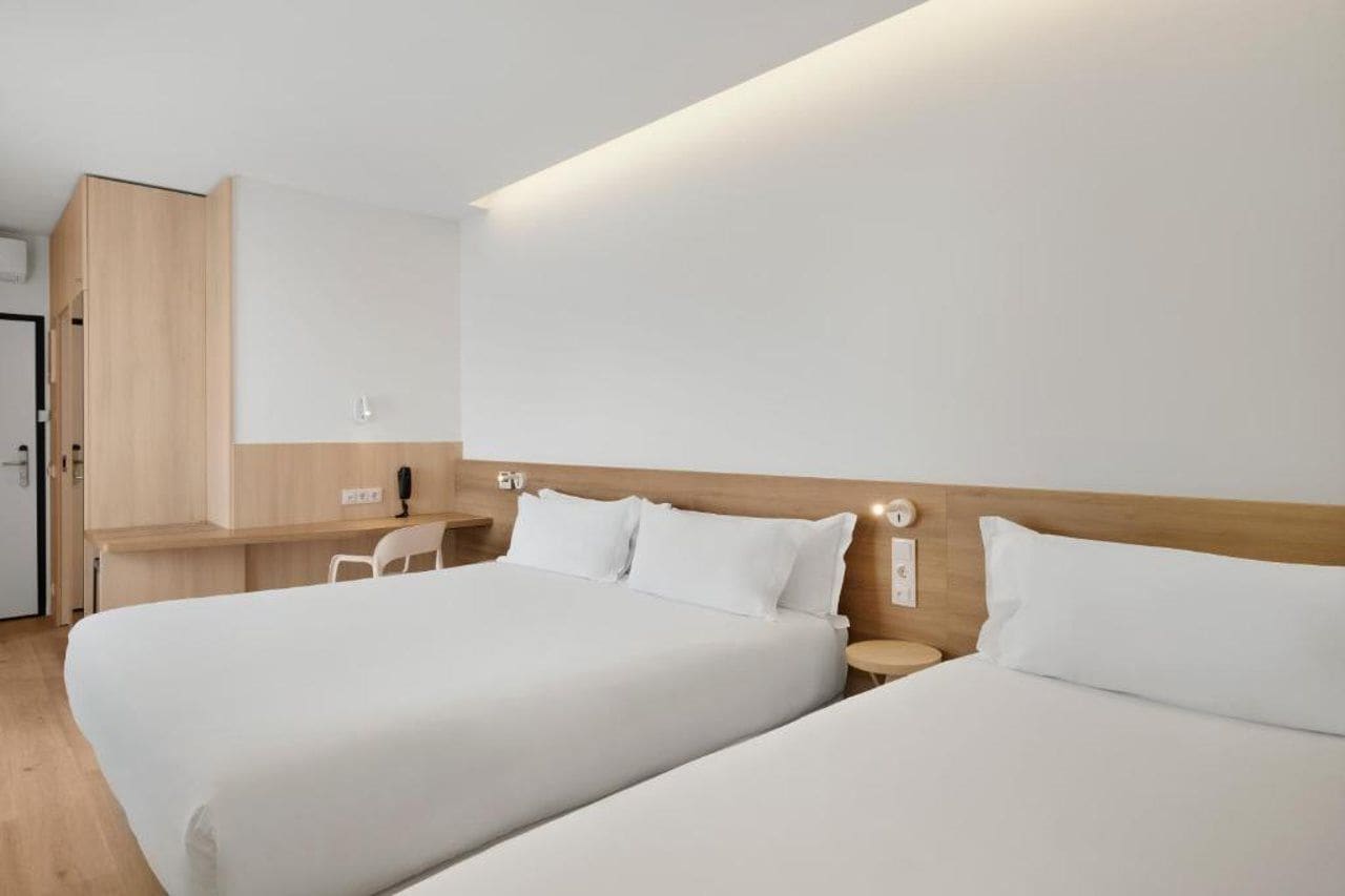 A hotel room with two beds, a desk, and a chair.