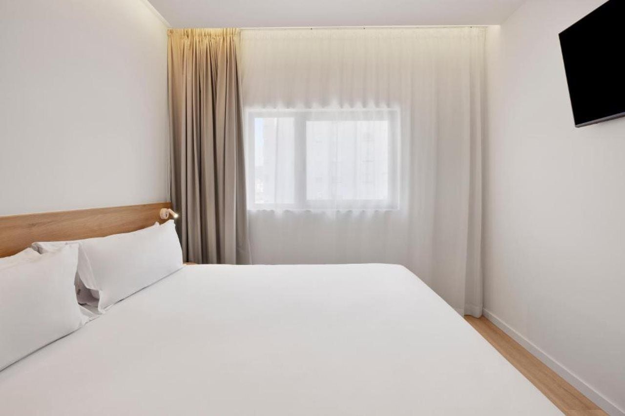 A hotel room with a bed, curtains, a window, and a wall-mounted television.