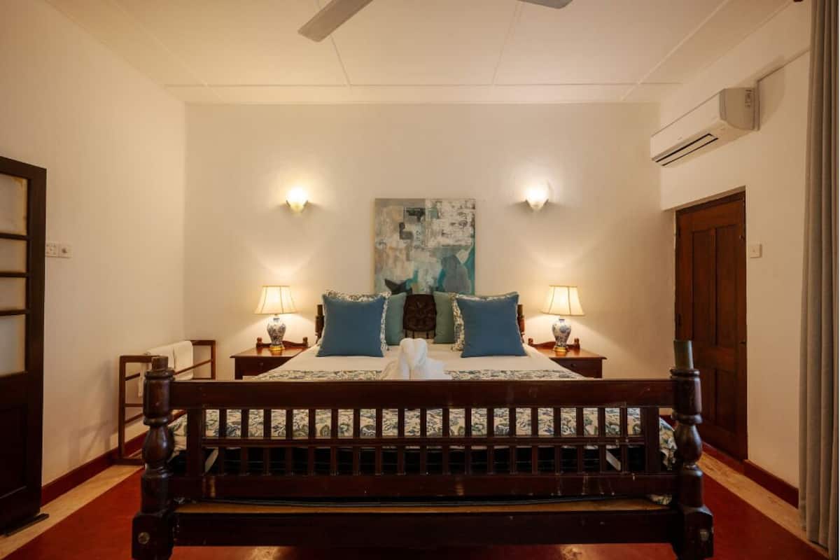 Une chambre avec un lit en bois, deux tables de chevet avec des lampes, un grand tableau abstrait accroché au mur et un appareil de climatisation fixé au mur.