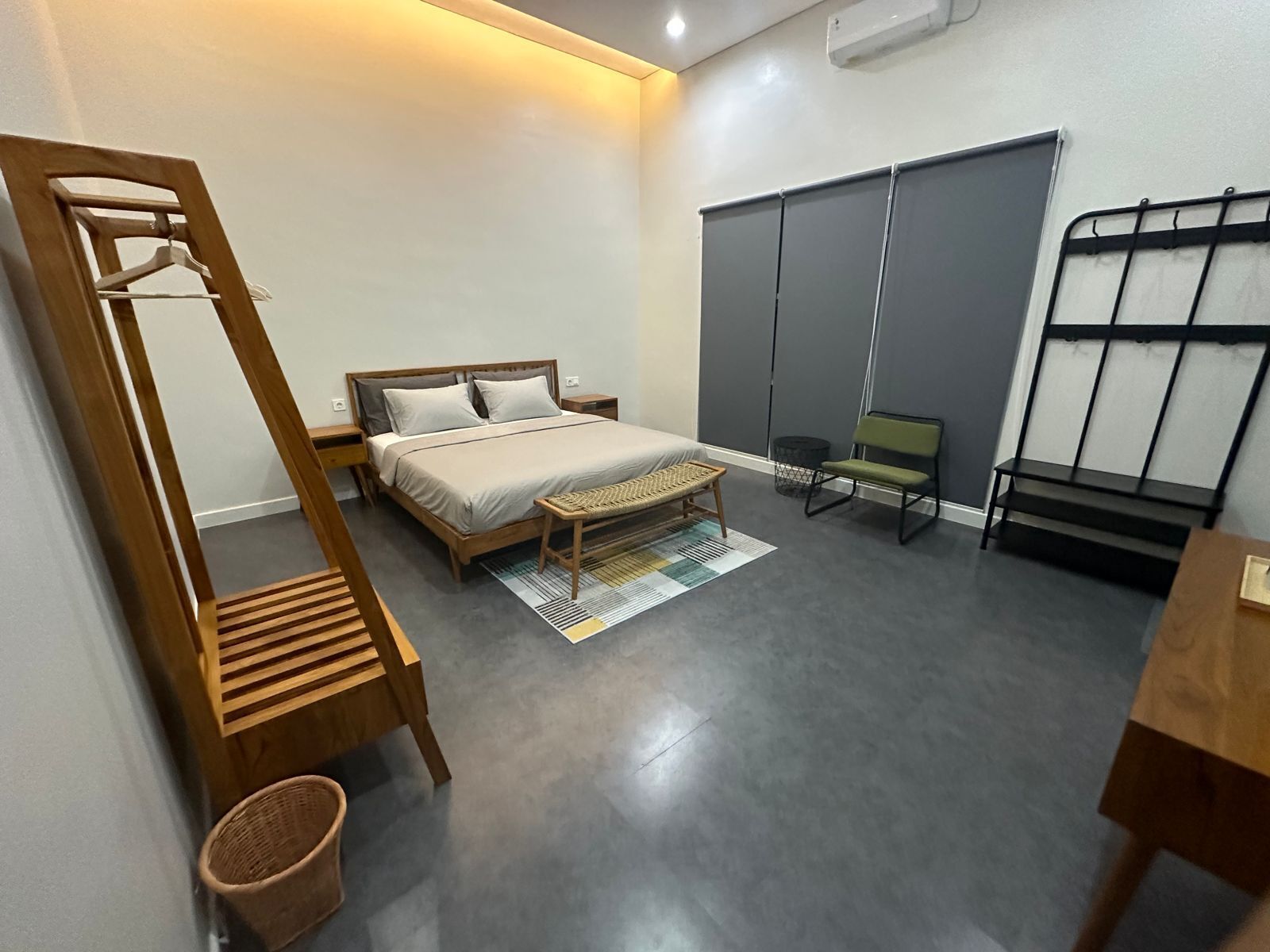 A bedroom with a bed, a wooden chair, a bench, a small table, and a wall-mounted rack.