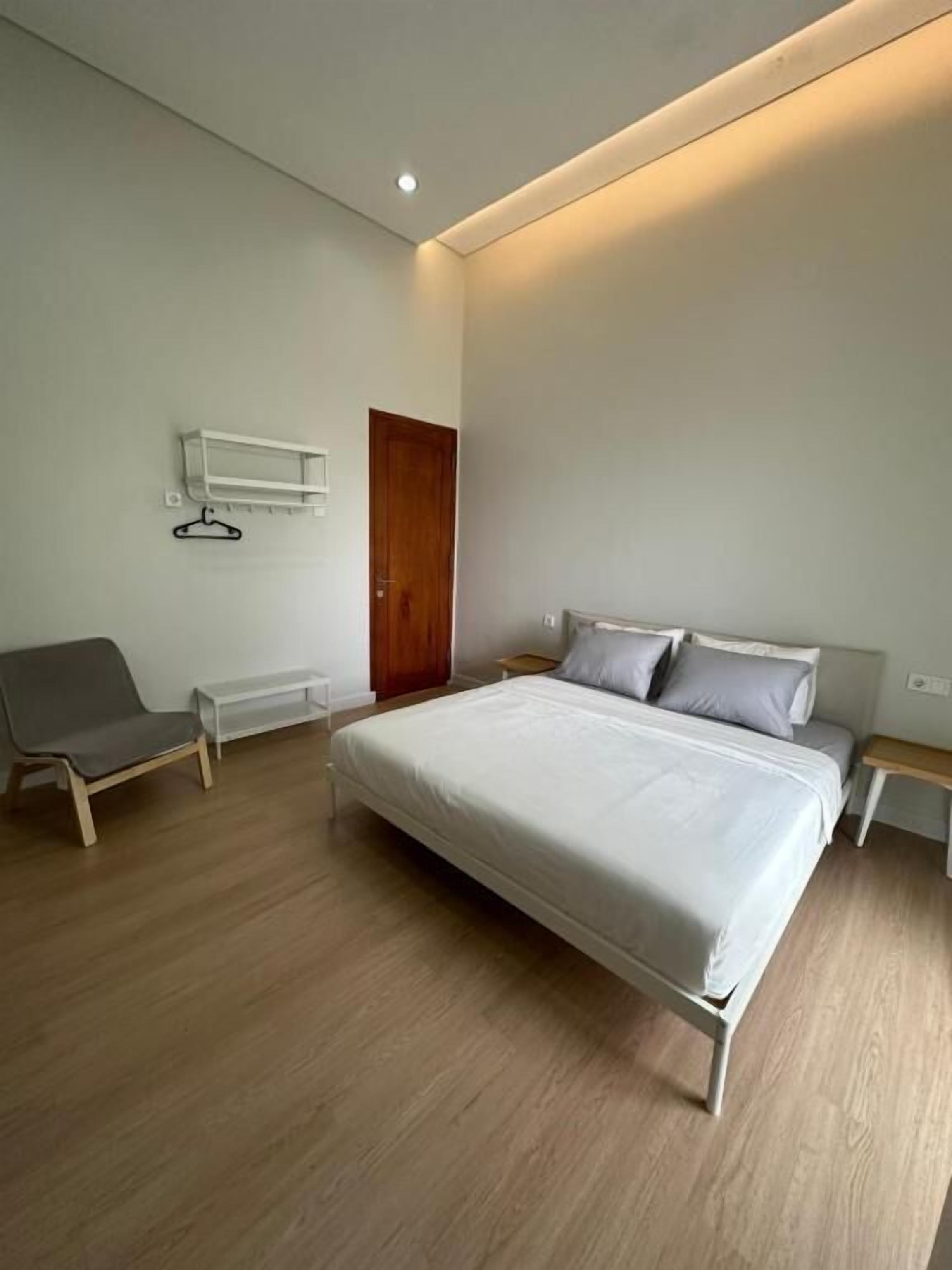 A modern bedroom with a large bed, a bedside table, a chair, and a wooden door.