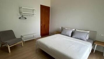 A modern bedroom with a large bed, a bedside table, a chair, and a wooden door.