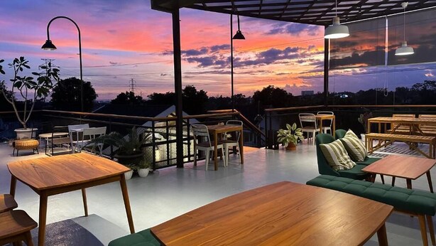An outdoor seating area with tables and chairs, a green sofa, and a view of the sunset. - Cendhani Raras Gallery (Depok)