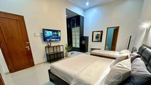 A modern hotel room with a large bed, a TV mounted on the wall, and a small seating area with a plant. - Cendhani Raras Gallery (Depok)