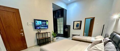 A modern hotel room with a large bed, a TV mounted on the wall, and a small seating area with a plant.