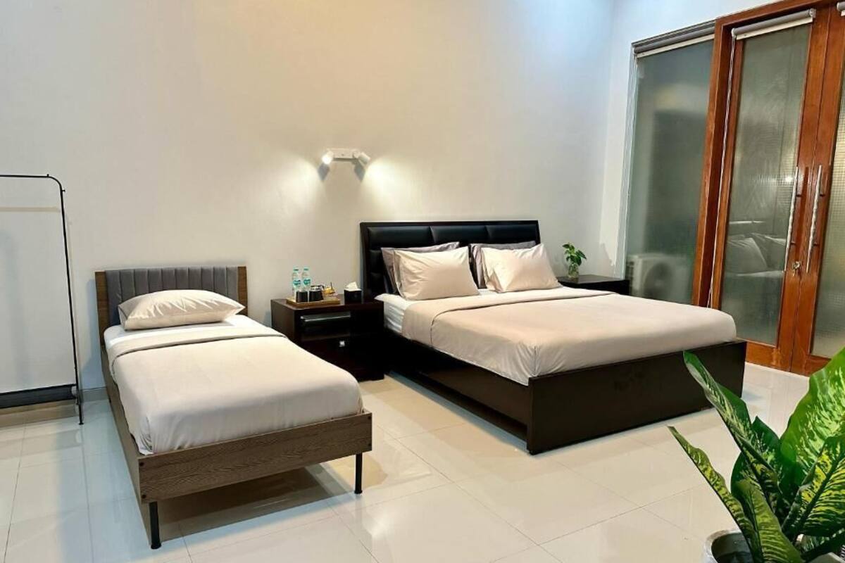 A modern bedroom with two beds, a bedside table with a lamp, and a large window with a view.