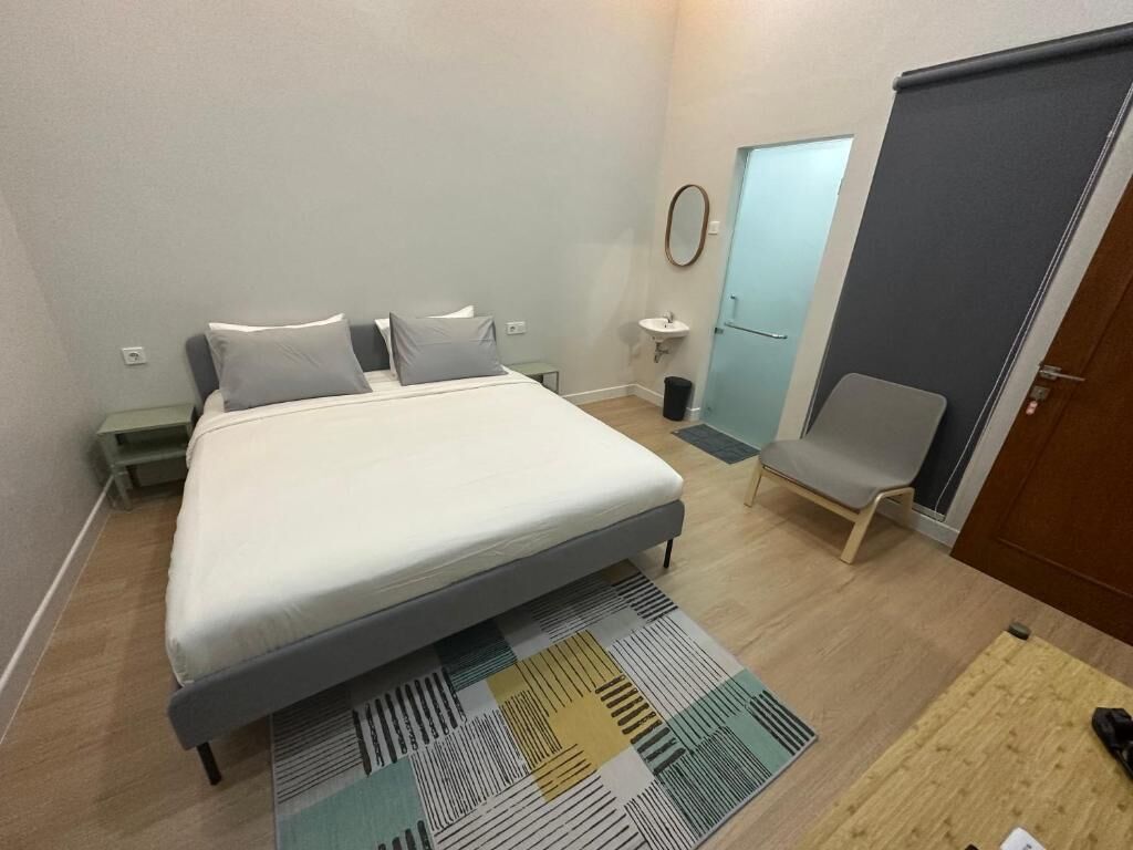 A bedroom with a bed, a chair, a small table, a sink, and a door.