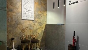 A reception area with a stone wall, a framed artwork, and a reception desk. - Cendhani Raras Gallery (Depok)