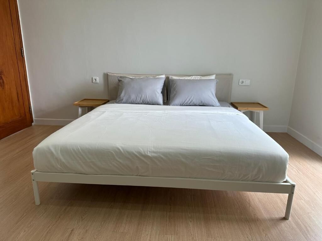 A single-bed room with a white mattress, two pillows, a wooden headboard, and two bedside tables.