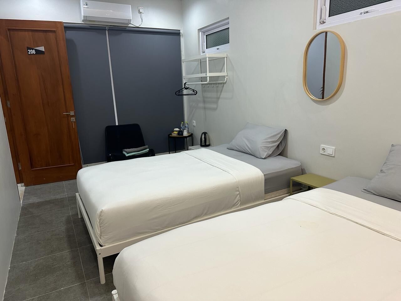 A hotel room with two beds, a wardrobe, a bedside table, a mirror, and a window.