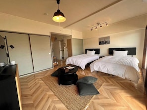 Moderni hotellihuone, jossa on kaksi sänkyä, sohva, sohvapöytä ja suuri peili.