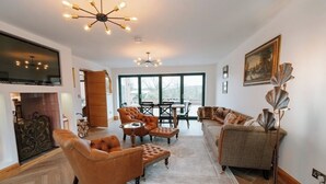 Uma sala de estar ampla com lareira, poltronas de couro, um sofá e uma área de jantar com uma grande janela que oferece uma vista.