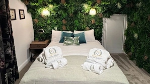 Quarto de hotel com cama, duas almofadas, mesa de cabeceira e parede coberta por vegetação.