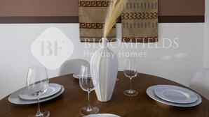 A dining table set with white plates and wine glasses, a white vase, and a decorative wall hanging. - Bloomfields Iconic 1Br In Marina (Abu Dhabi)