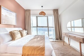 A modern bedroom with a large bed, a city view through the window, a bedside table, and a mirror. - Bloomfields 1BR in Marina Blue-Reem (Abu Dhabi)