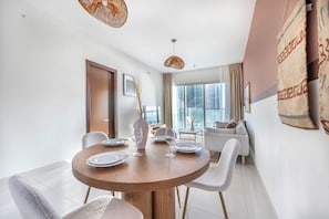 A modern dining area with a round wooden table, white chairs, and a vase with a tall plant. - Bloomfields 1BR in Marina Blue-Reem (Abu Dhabi)