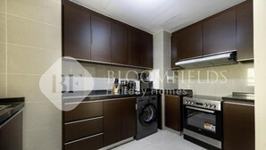 A modern kitchen with dark cabinets, a washing machine, and a built-in oven. - Bloomfields Iconic 1Br In Marina (Abu Dhabi)