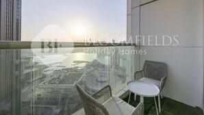 A balcony with wicker chairs and a small table, overlooking a cityscape with a body of water and buildings. - Bloomfields Iconic 1Br In Marina (Abu Dhabi)