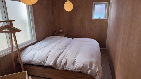 A bedroom with a bed, a bedside table, a lamp, and a window.