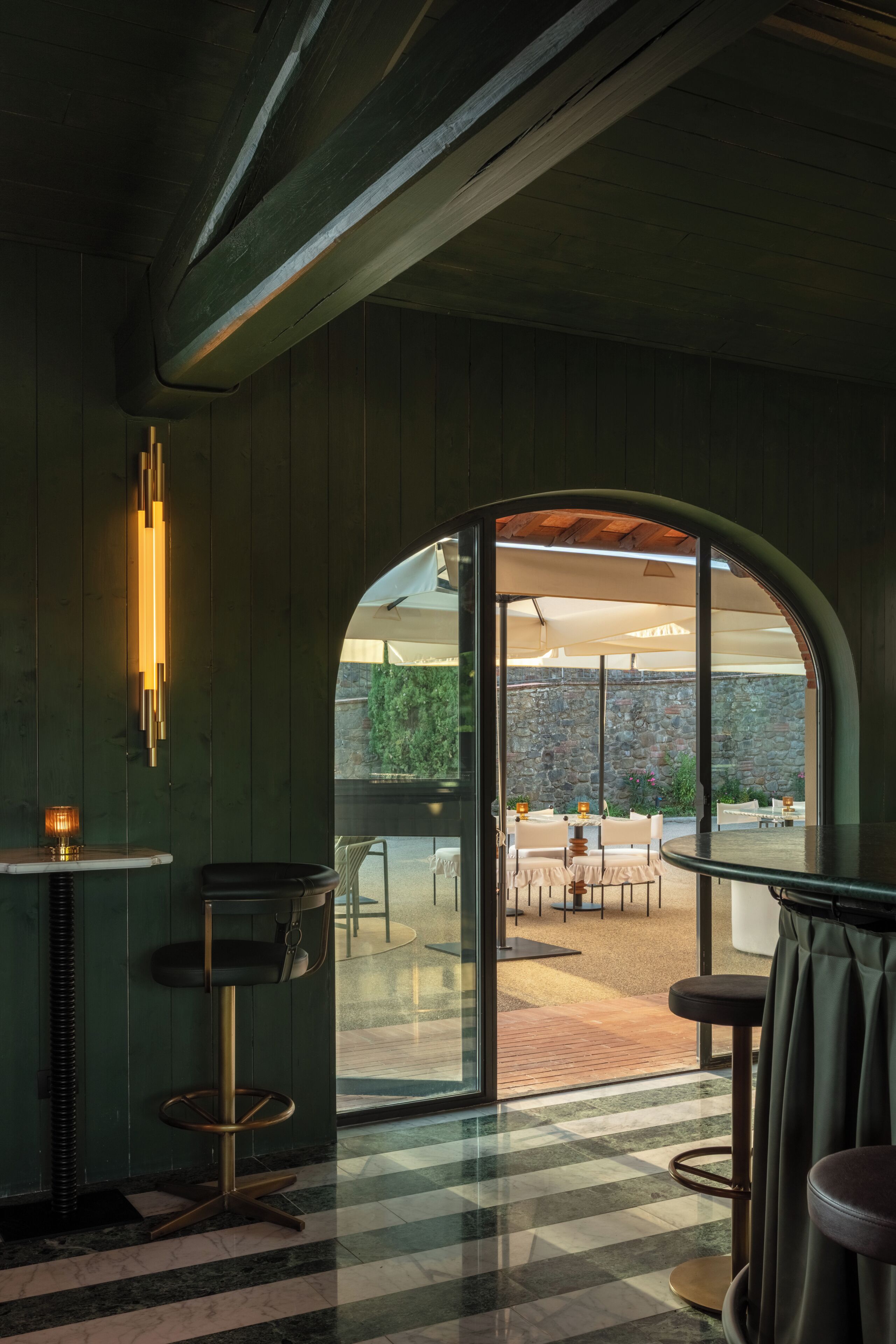 An interior space with a bar area, seating, and a view through an arched doorway to an outdoor patio.