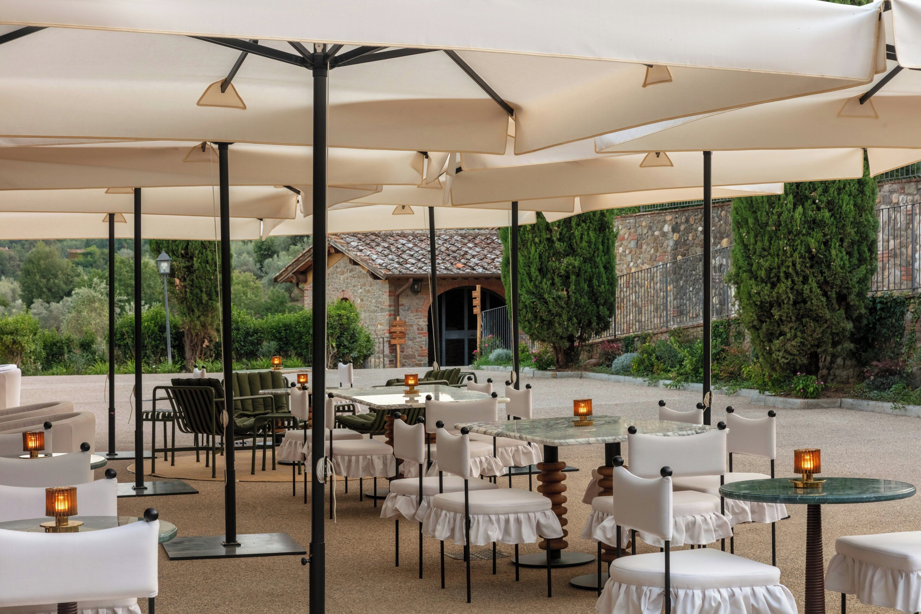 An outdoor seating area with tables and chairs, covered by umbrellas, and a stone building in the background.