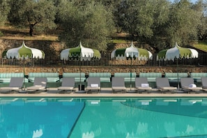 Un área junto a la piscina con sillones de descanso y sombrillas.