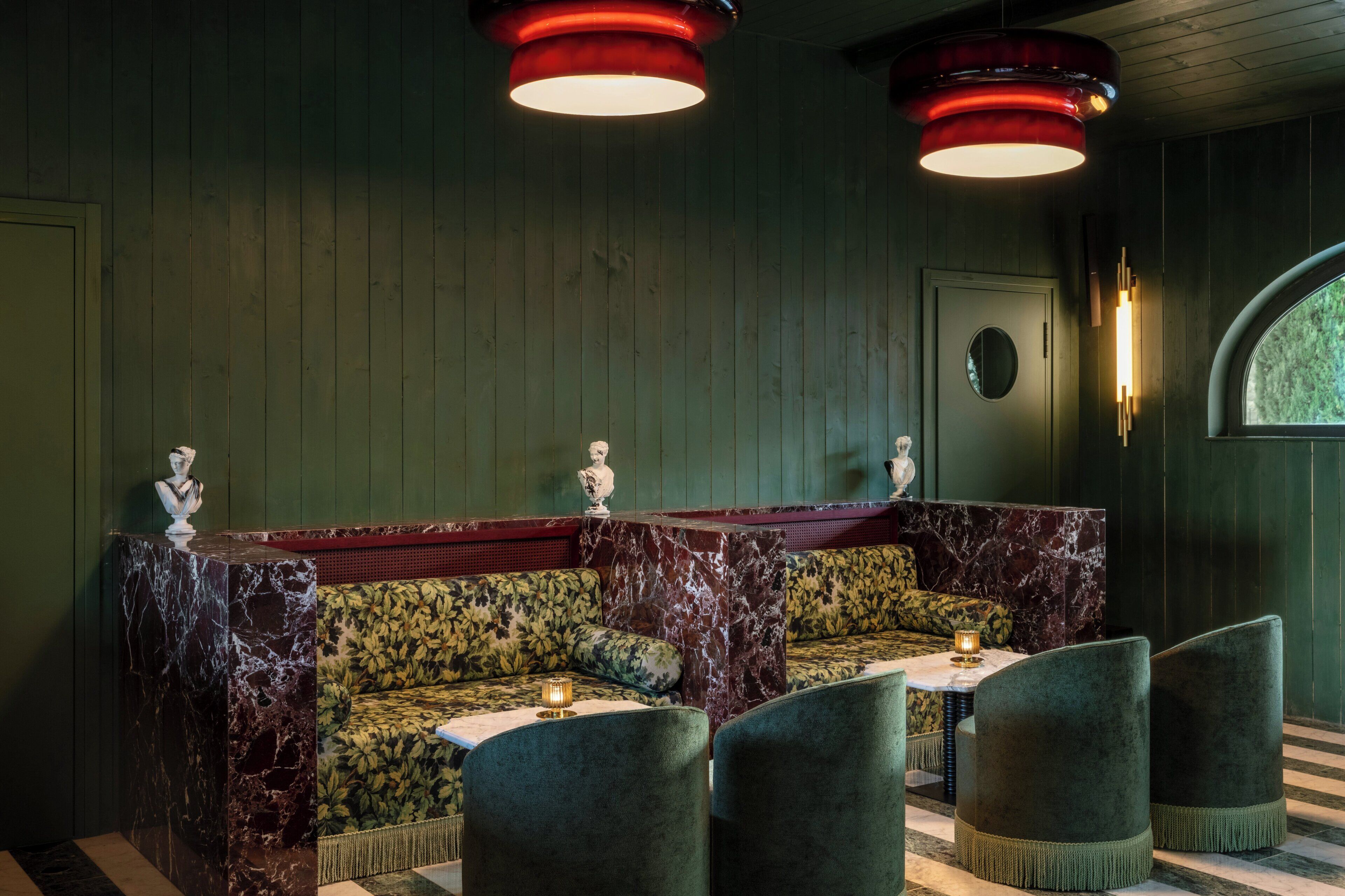 A room with a green upholstered bench, marble-topped tables, and green upholstered chairs.