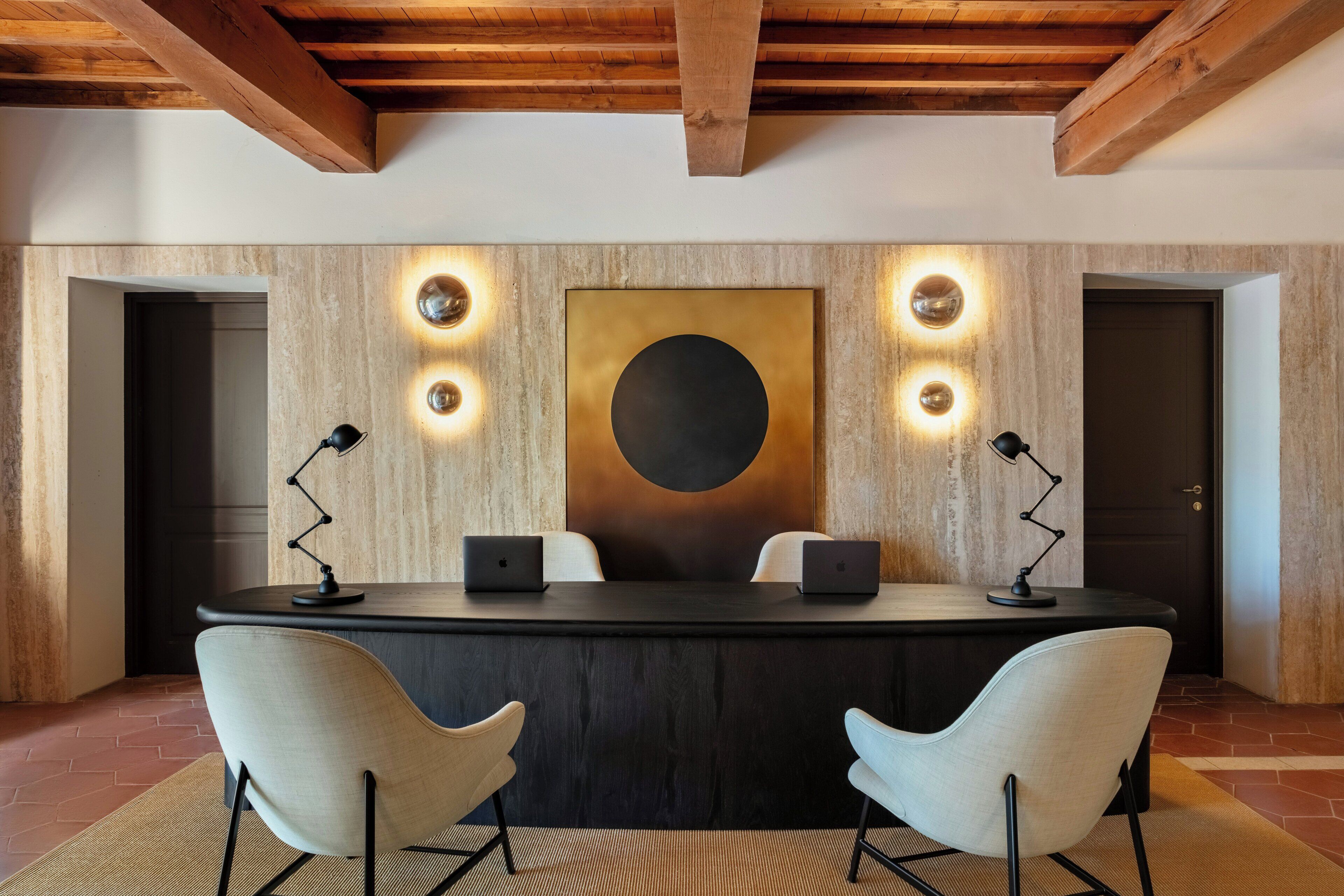 A conference room with a dark table, two chairs, a large abstract painting, and wall-mounted lights.