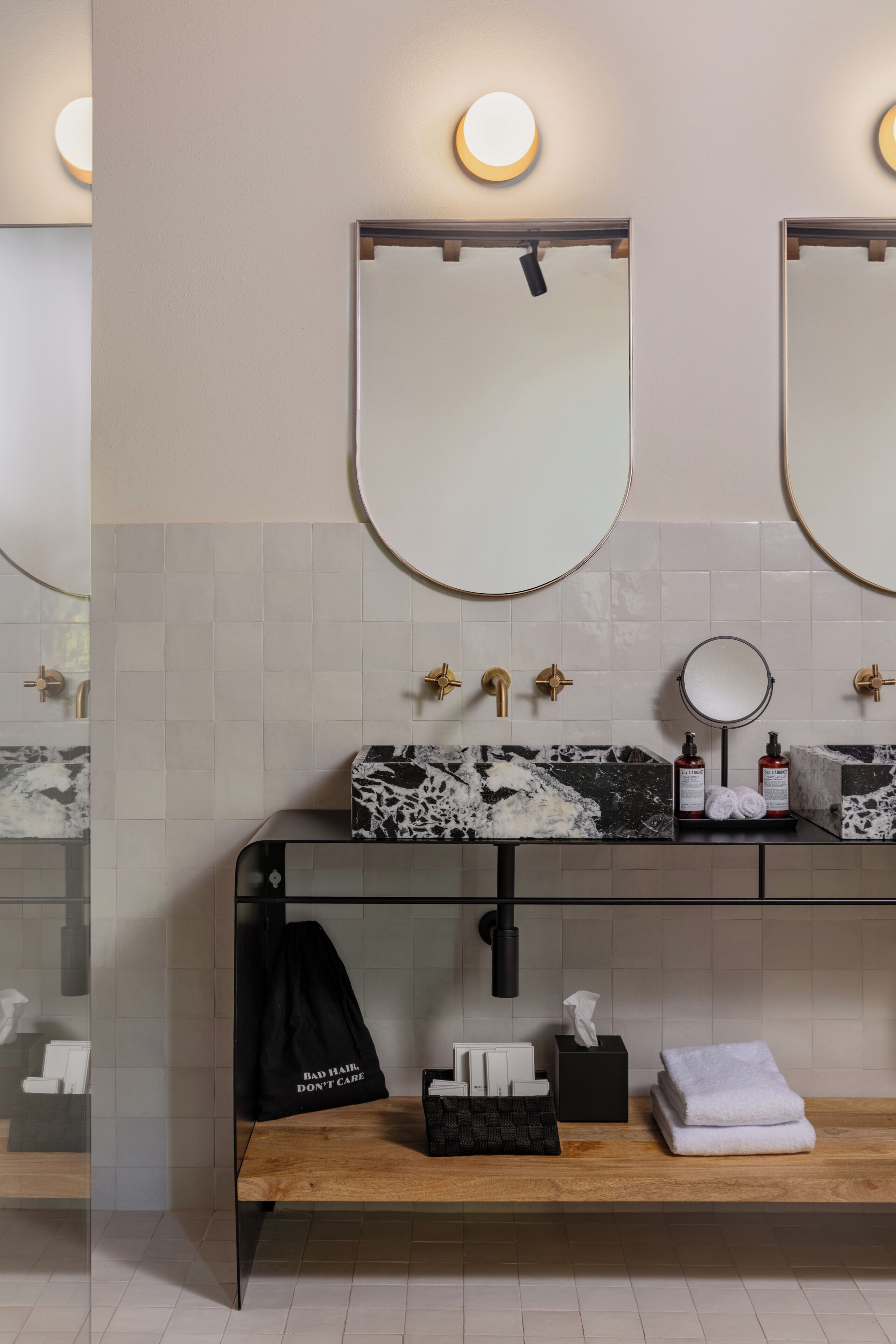 Un bagno moderno con un lavello in marmo nero, rubinetti dorati e uno specchio rotondo sopra.