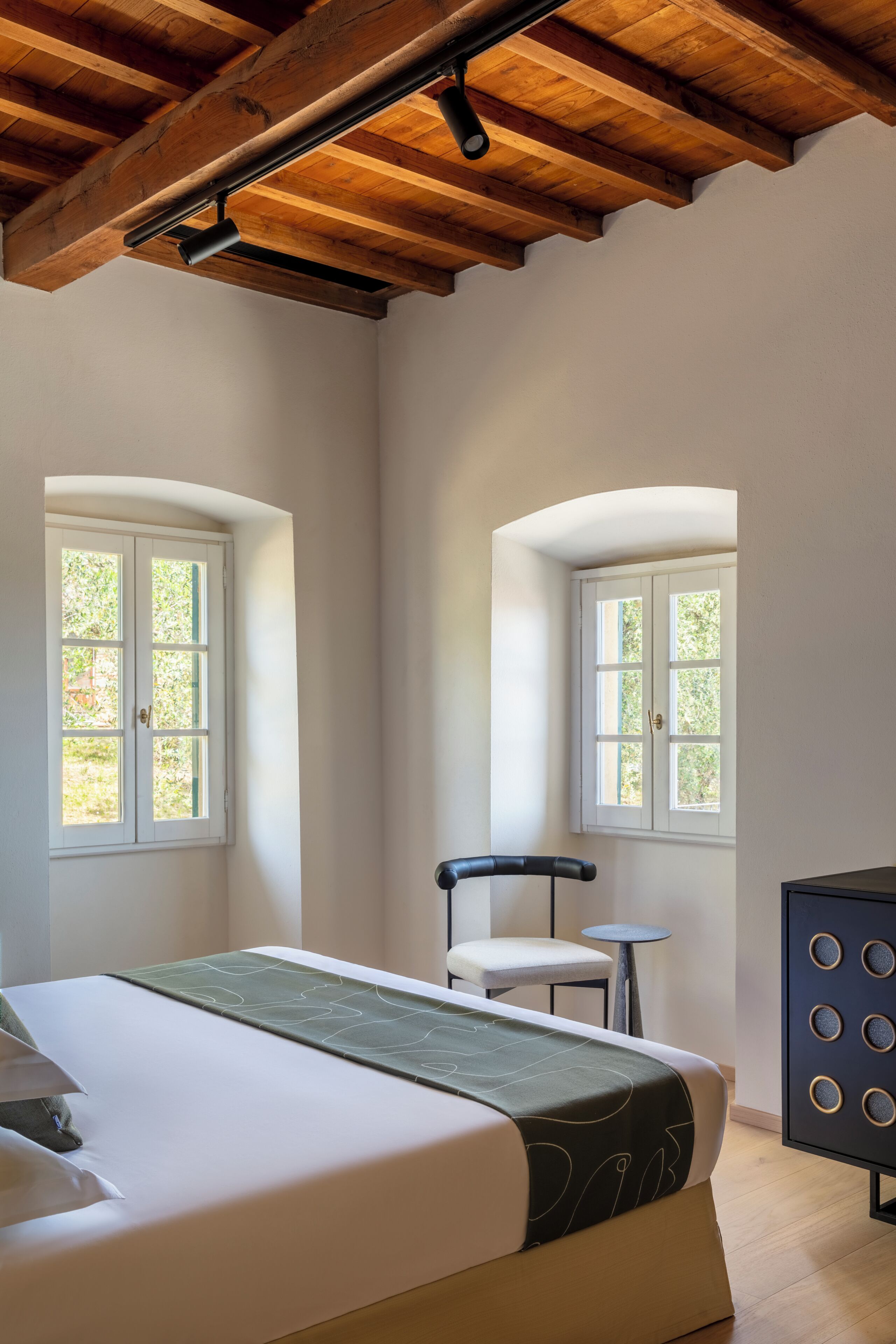 A bedroom with a bed, two windows, a chair, and a dresser.