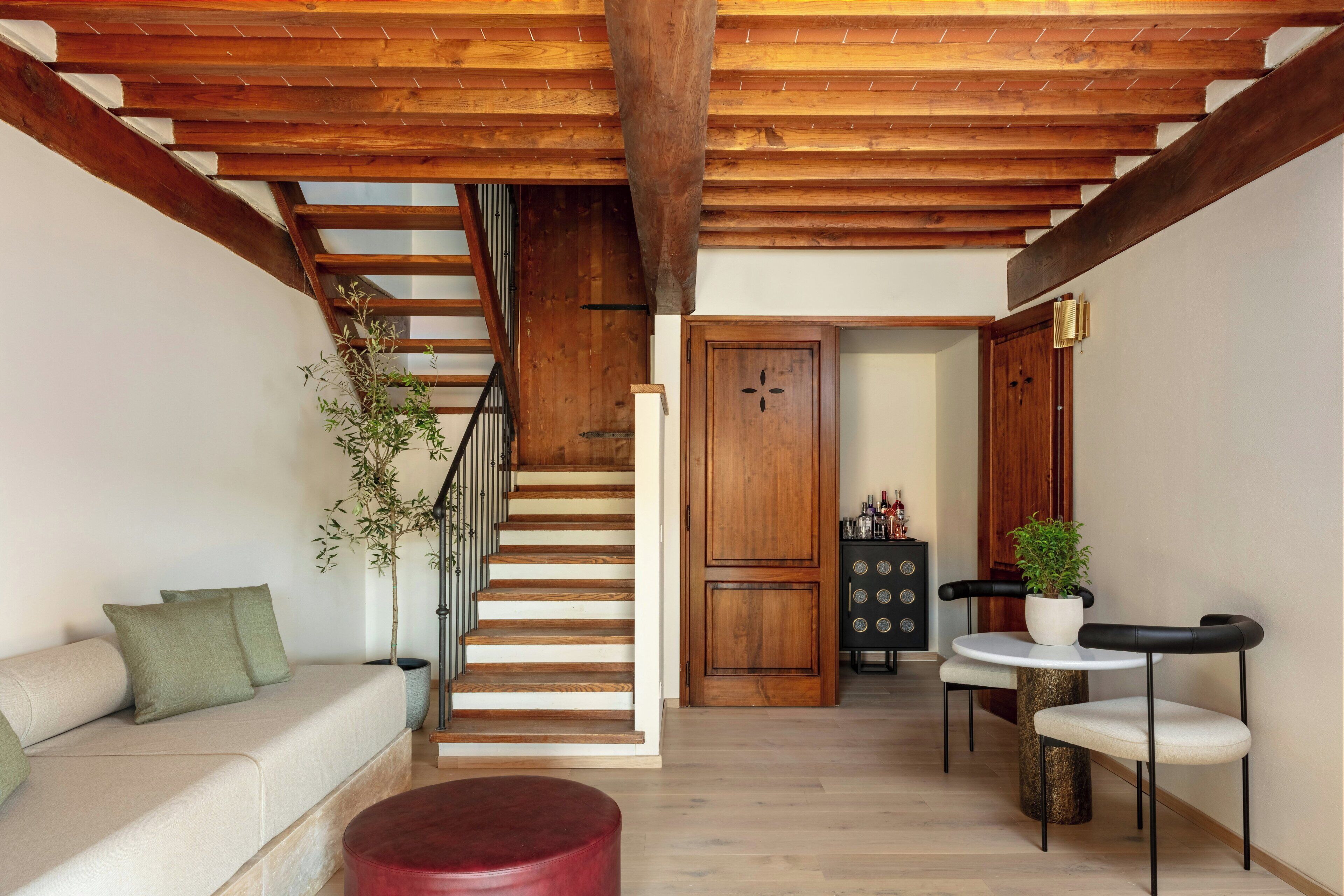 Un vaste espace de vie comprenant un escalier en bois, un canapé, un pouf rouge, une table à manger avec des chaises et une plante en pot.