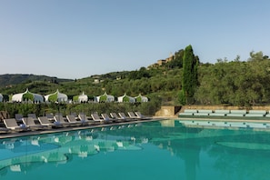 A swimming pool with lounge chairs and umbrellas, surrounded by greenery and hills. - Chapter Chianti, a Member of Design Hotels (Cavriglia)
