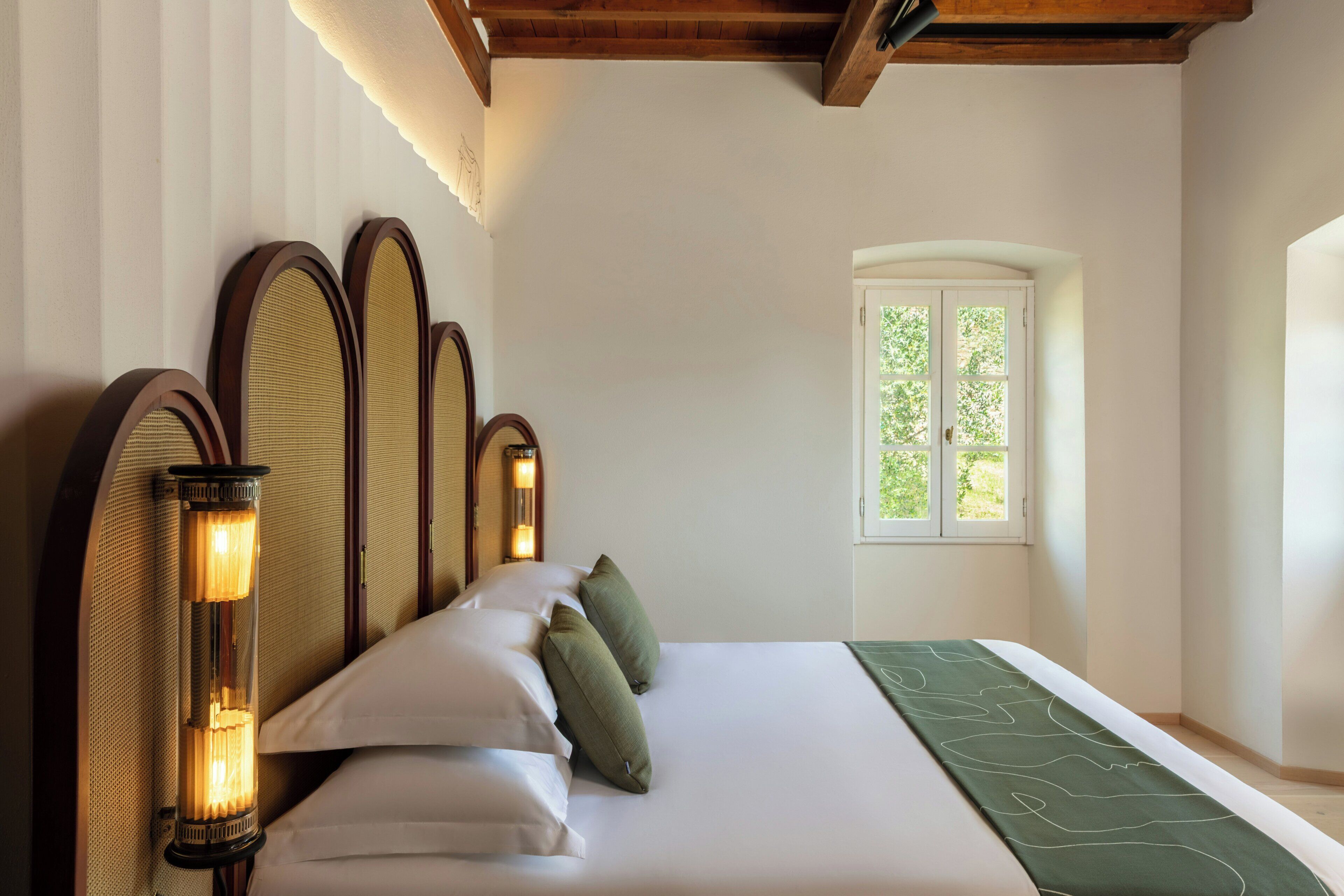 A room with a bed, a window, and a wall-mounted lamp.