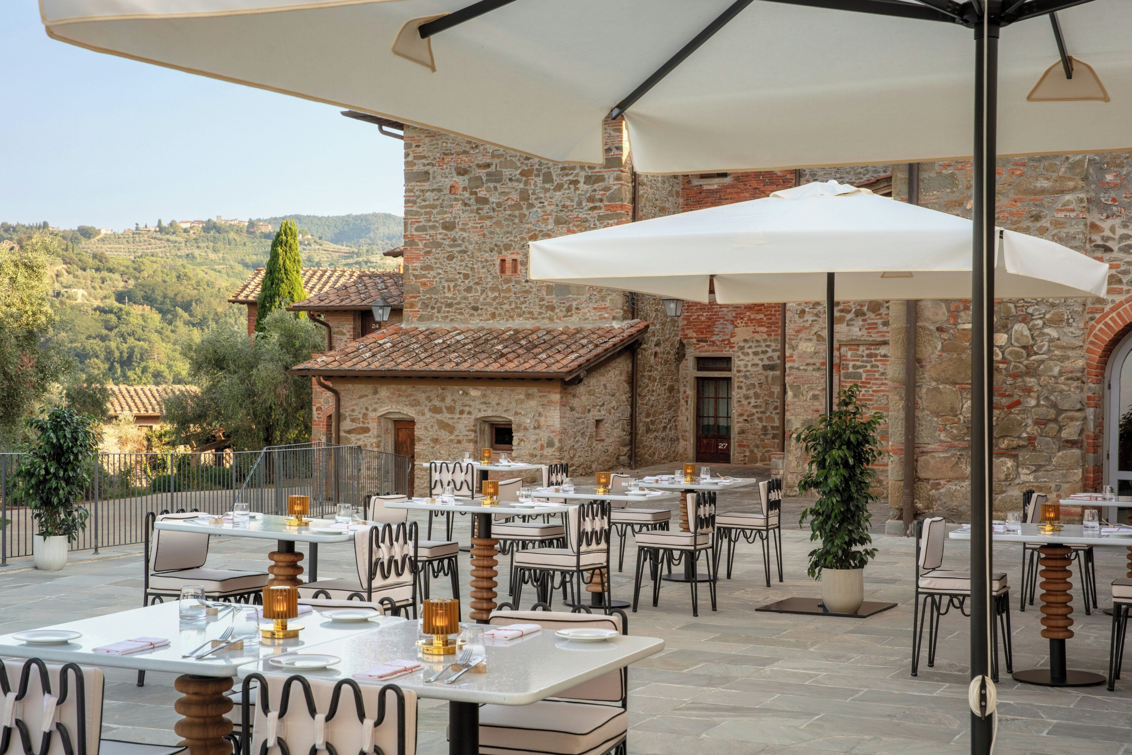 An outdoor dining area with stone walls, tables, chairs, and umbrellas.