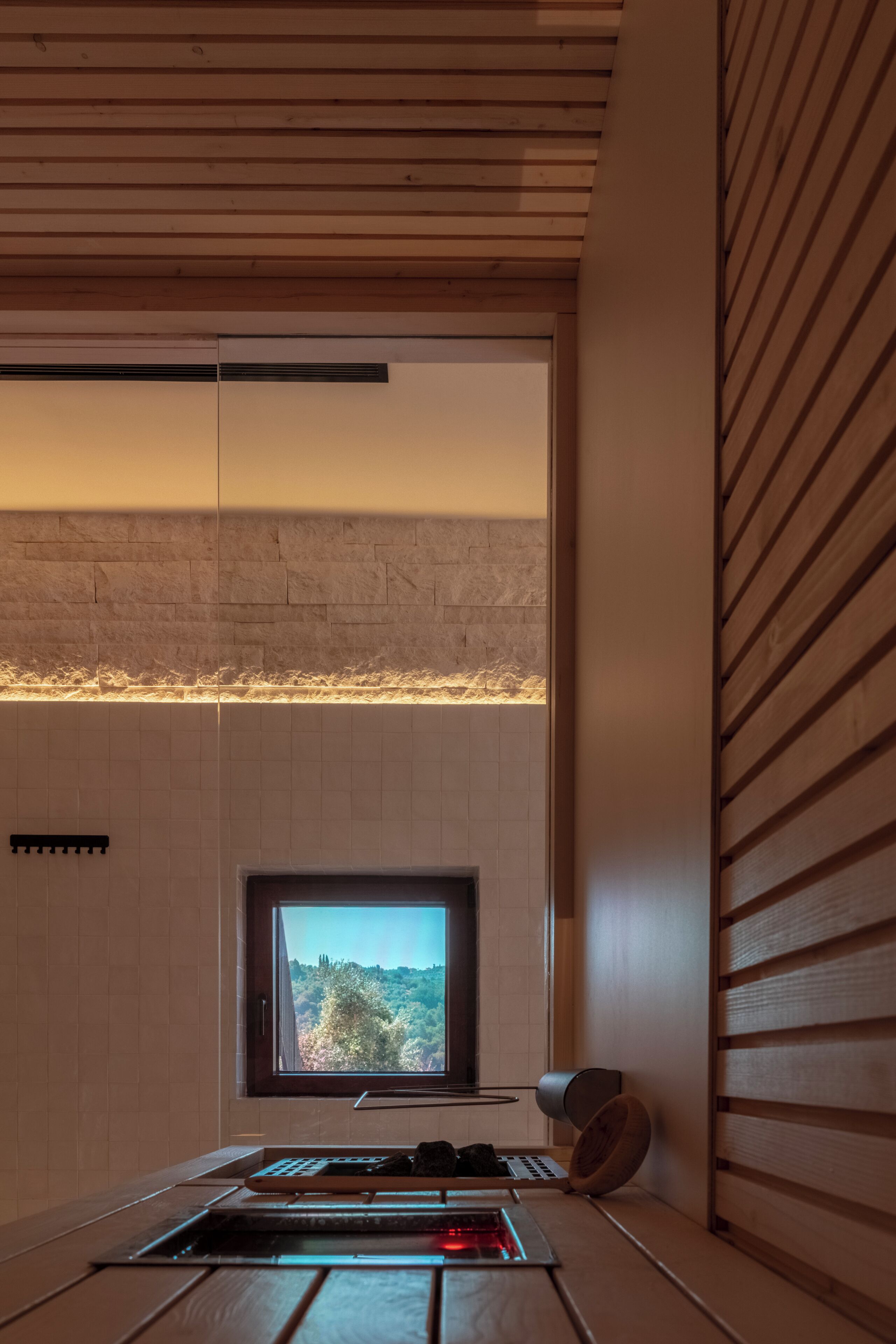 A modern kitchen with a large window, wooden ceiling, and a view of a forested area.