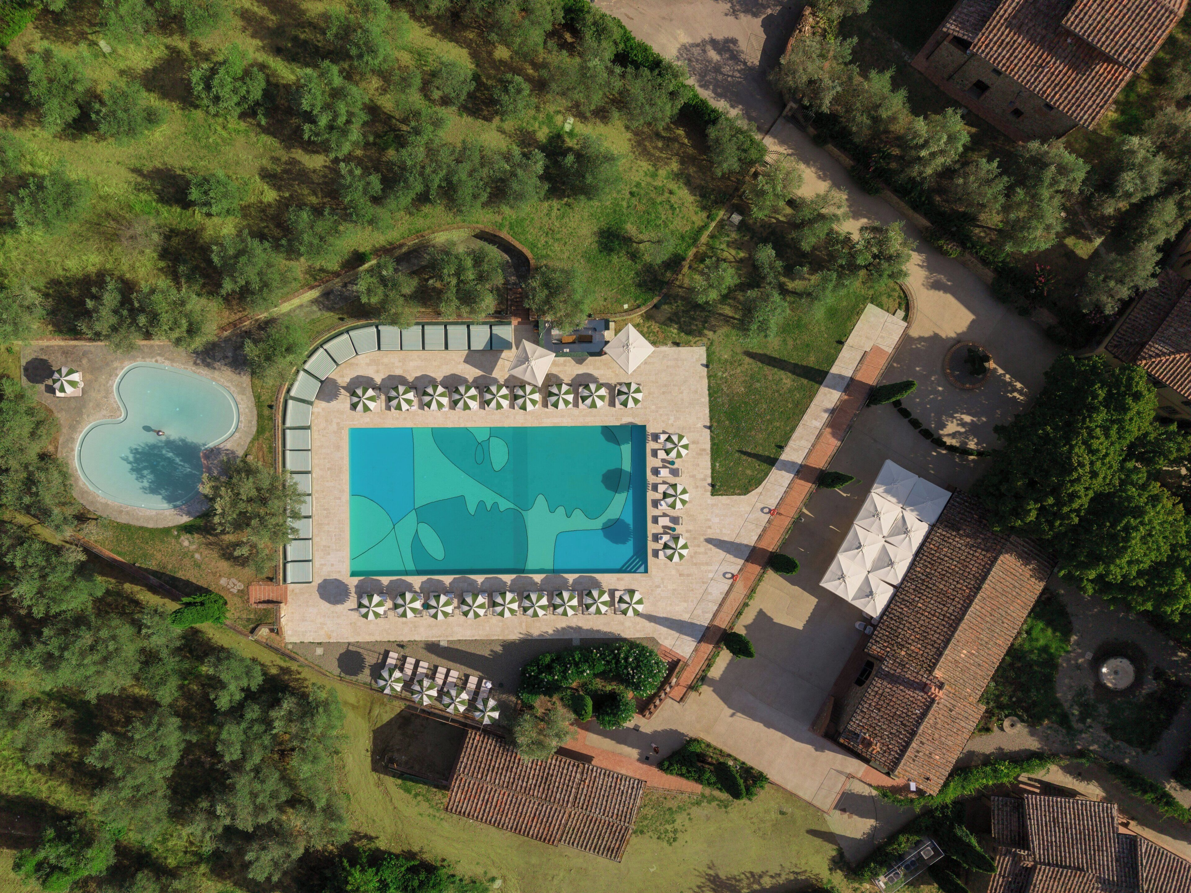 Eine Luftaufnahme eines Resorts mit einem Schwimmbad, Liegestühlen und einem kleinen, kreisförmigen Pool.