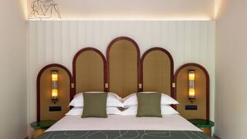 Una habitación de hotel con una cama grande, dos mesitas de noche, un cabecero con varios paneles y lámparas fijadas a la pared.