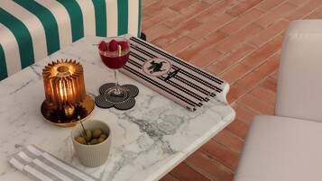 Uma mesa de mármore com uma lâmpada decorativa, um copo de bebida vermelha com framboesas, uma tigela de azeitonas e um guardanapo riscado.