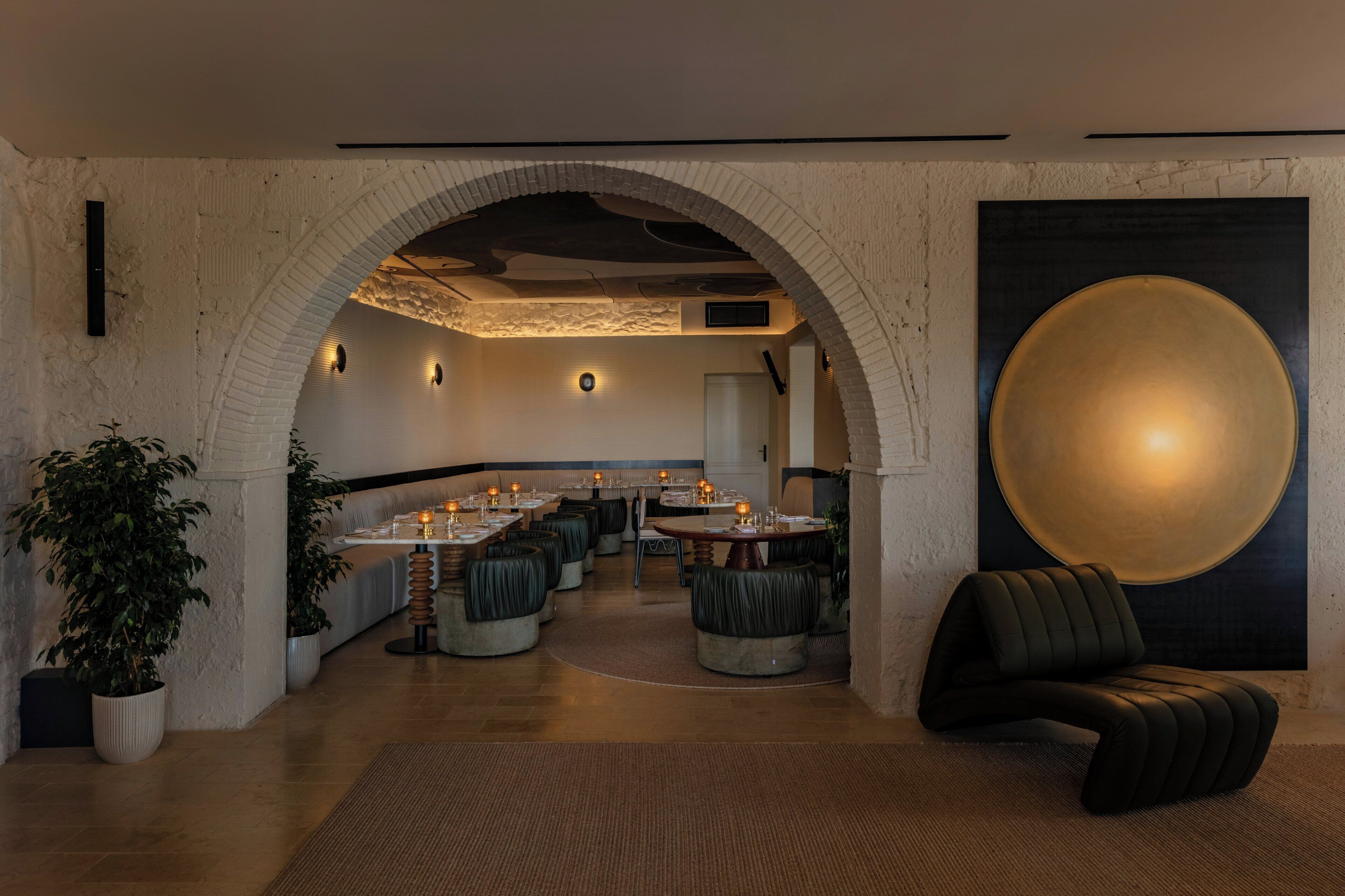 Un interior moderno con un arco que da a un comedor con mesas redondas y asientos acolchados.