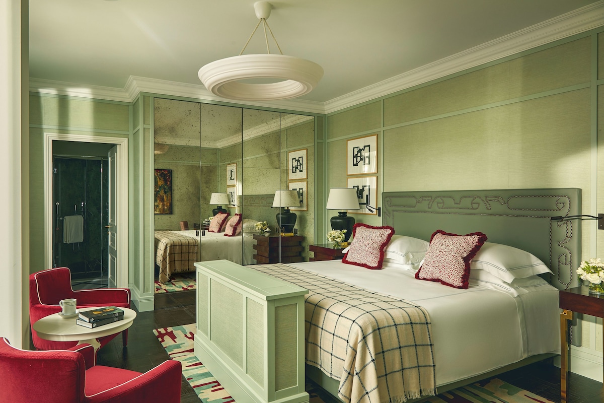 A hotel room with a bed, a desk, a chair, a mirror, and a door.