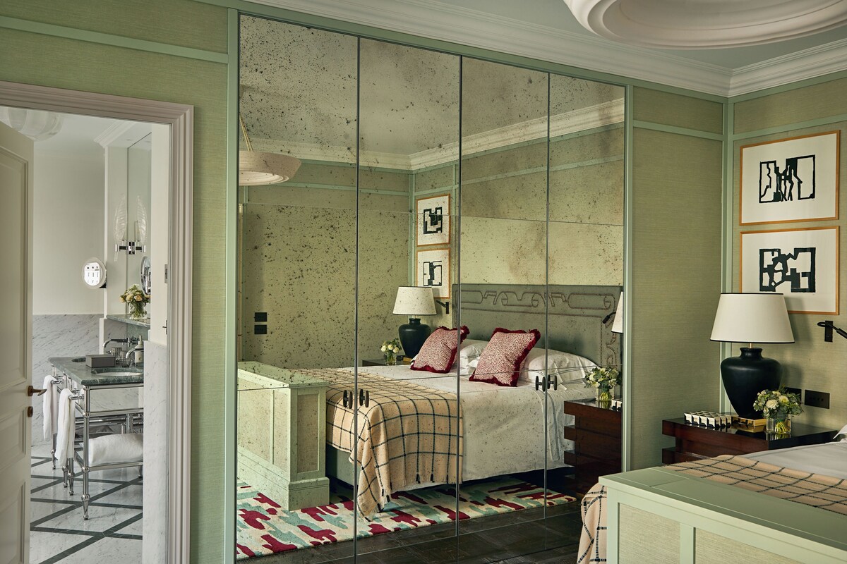 A bedroom with a large mirror, a bed with a headboard, bedside tables, and a nightstand with a lamp.