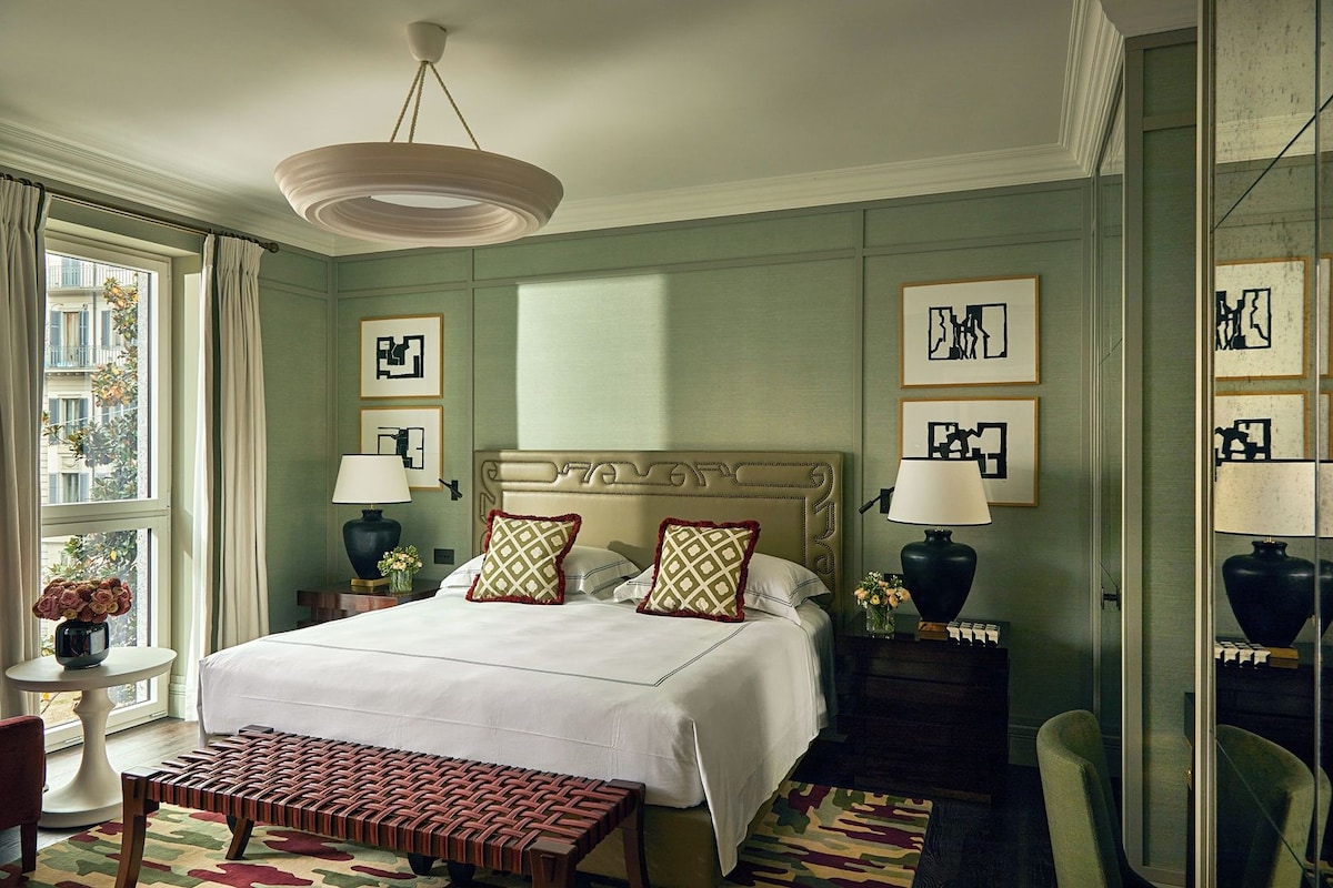 A hotel room with a large bed, two bedside tables with lamps, a bench, and artwork on the walls.