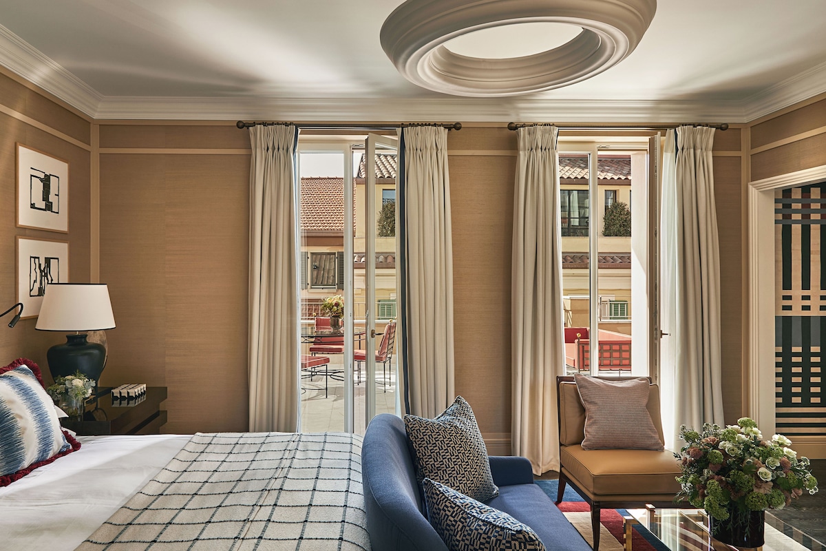 A hotel room with a bed, a sofa, a table with a lamp, and a view of the outside.