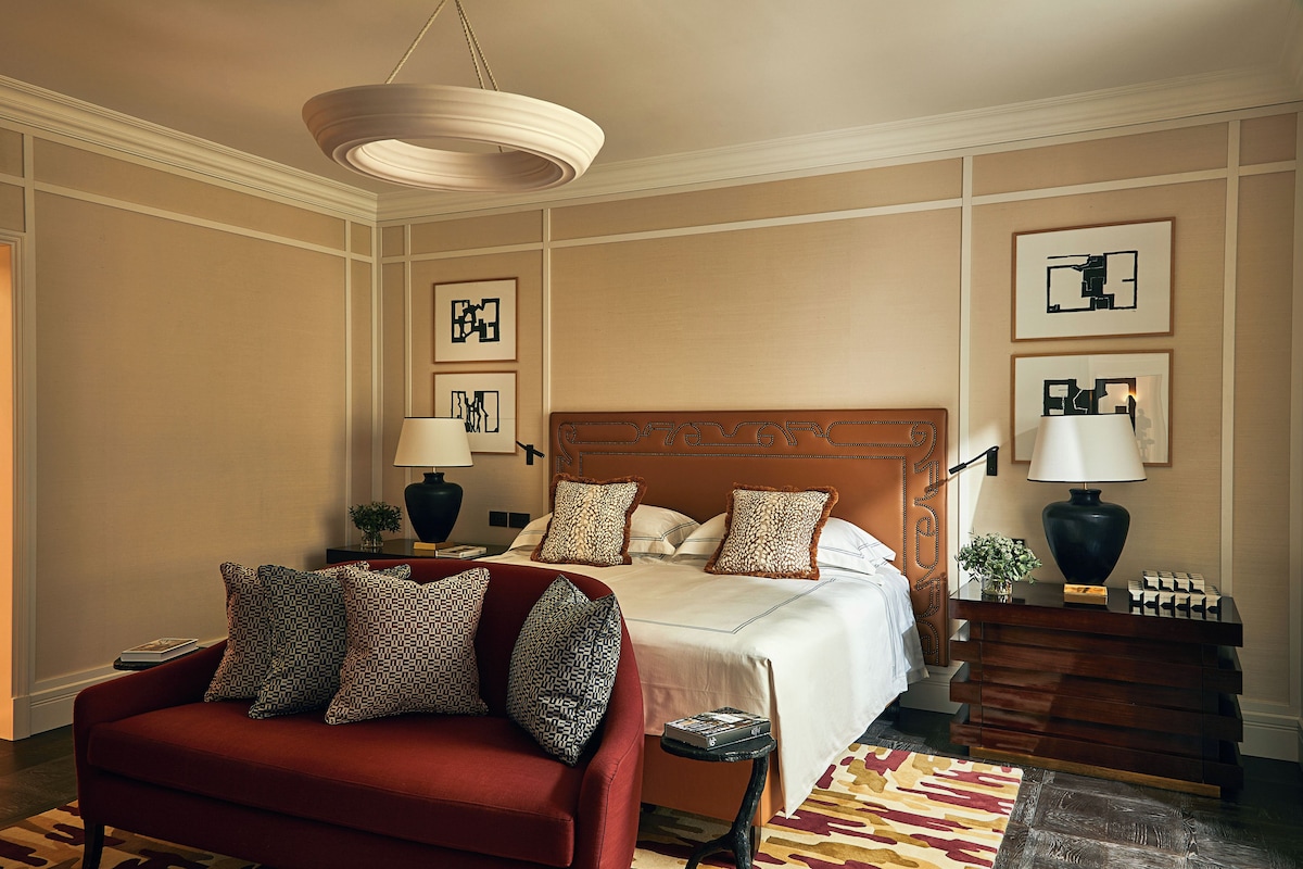 A hotel room with a large bed, a red sofa, a wooden nightstand, and a hanging light fixture.