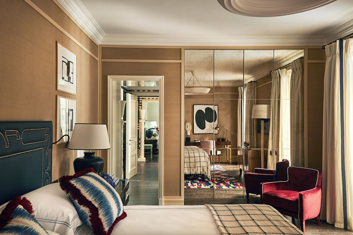 A hotel room with a bed, a desk, a chair, and a large mirror.
