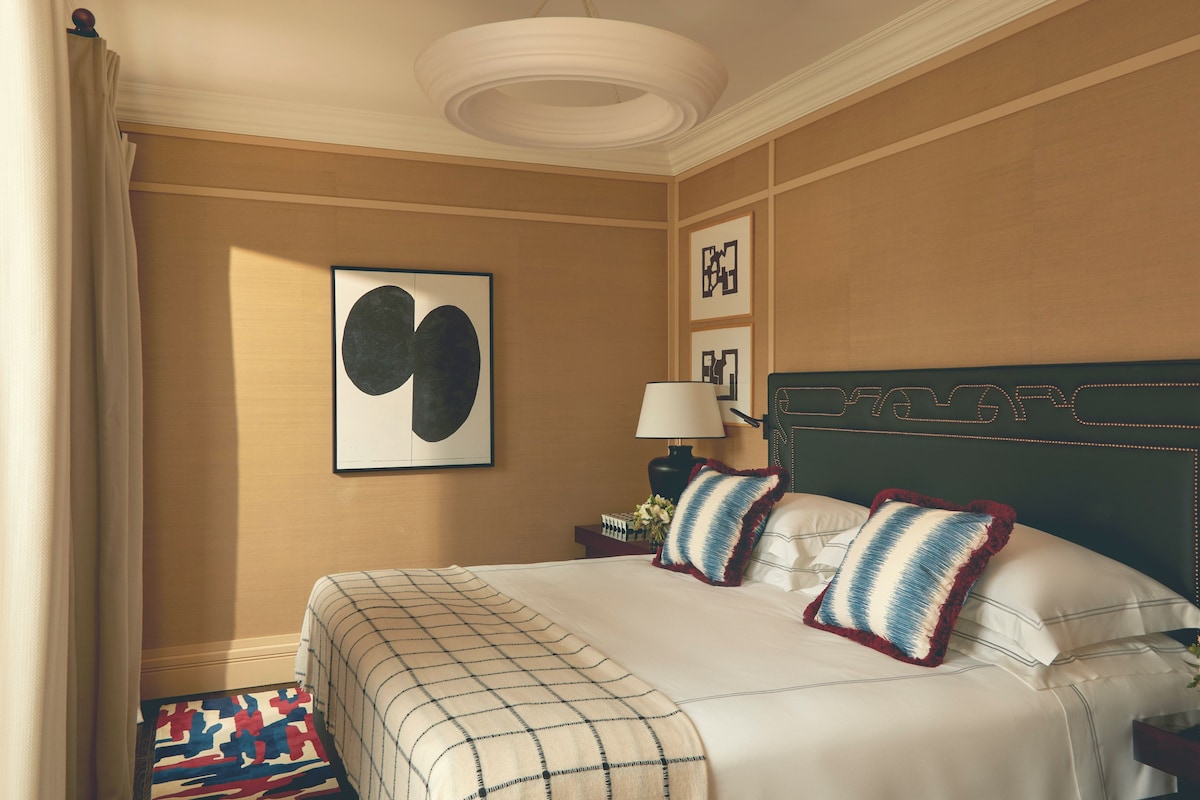 A hotel room with a large bed, a nightstand with a lamp, and a wall with framed artwork.