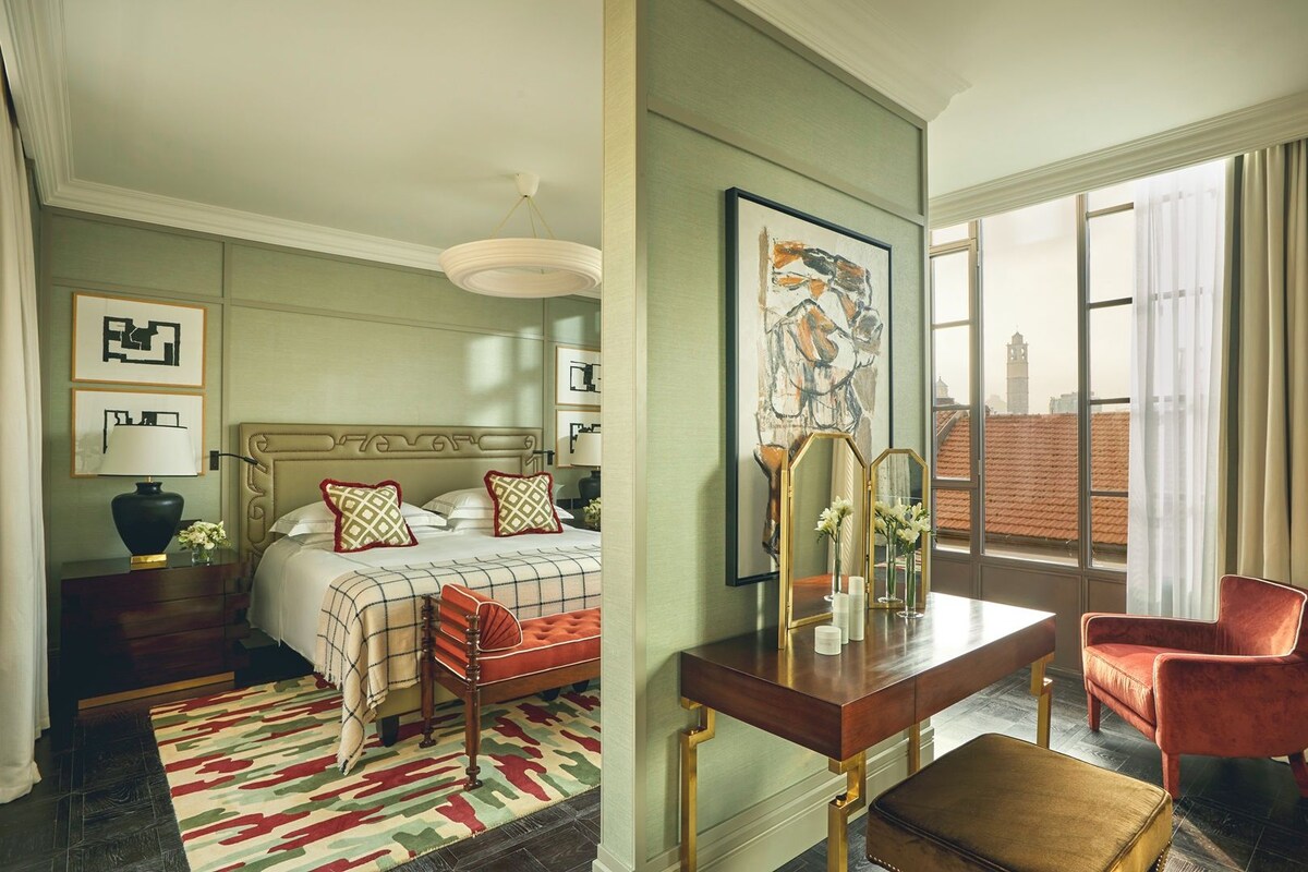 A hotel room with a bed, bedside table, lamp, and a large window with a view.