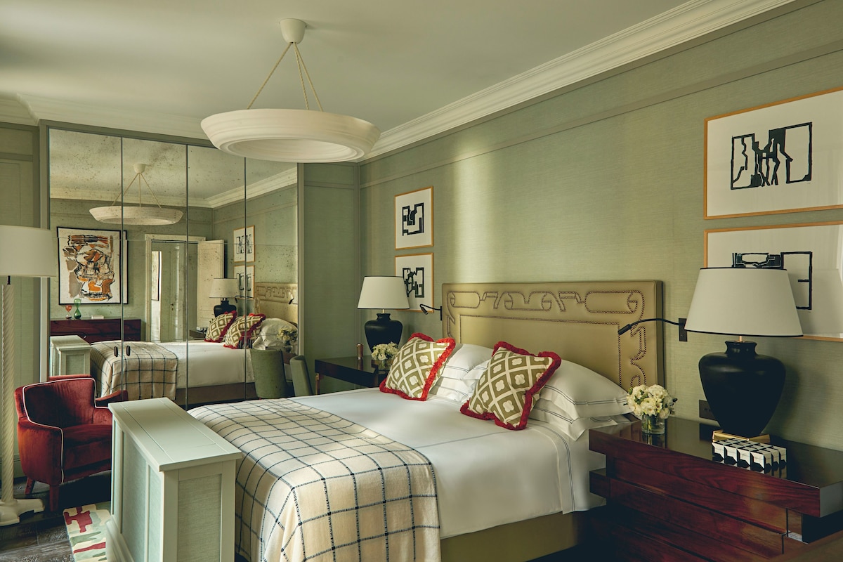 A hotel room with a large bed, two bedside tables, a chair, a mirror, and artwork on the walls.