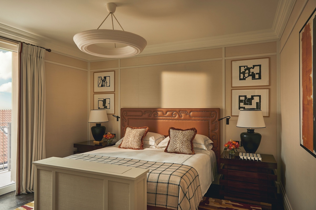 A hotel room with a large bed, two bedside tables with lamps, a ceiling light, and framed artwork on the walls.